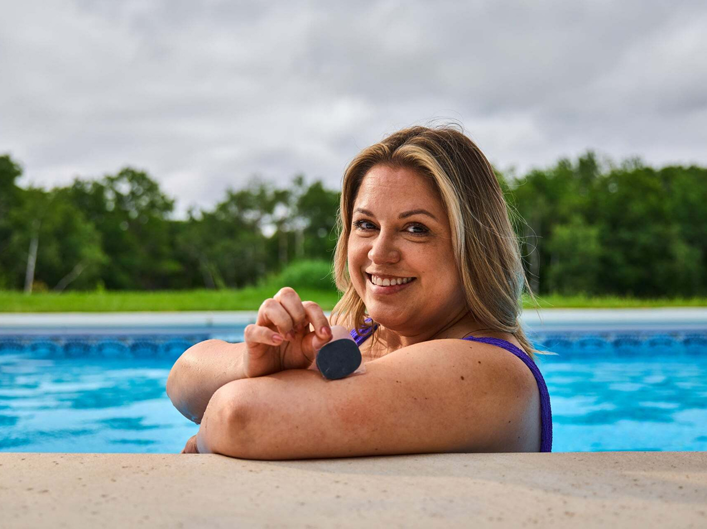 Eversense user smiling, flexing arm with a CGM sensor device attached, seated on a blue chair.