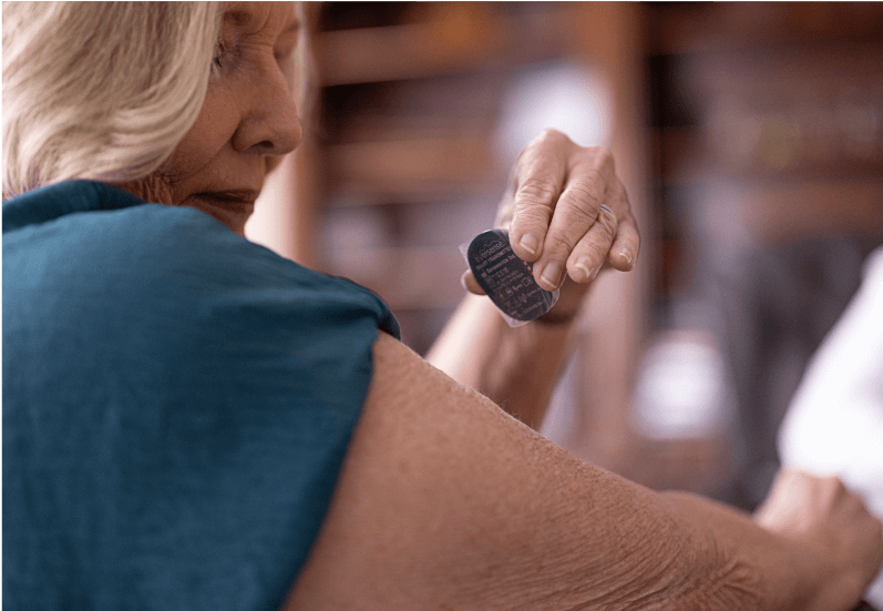 Woman applies removable CGM transmitter to upper arm in a cozy, home setting